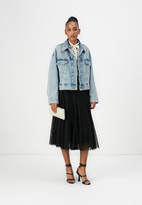 Lichtblauwe spijkerjas met borstzakken, zwarte tule rok, witte blouse met stippen en een gestreepte clutch. Zwarte sandalen met hoge hakken.