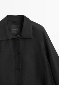 Schwarzes Hemd mit Knopfleiste, spitzem Kragen, langen Ärmeln und einem sichtbaren "Massimo Dutti"-Etikett im Nackenbereich.