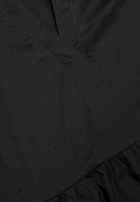 Schwarzer Stoff mit glatter Textur und leichtem Glanz. Verfügt über ein V-Ausschnitt-Design und eine geraffte Rüsche am Saum. Die Nähte sind sichtbar.