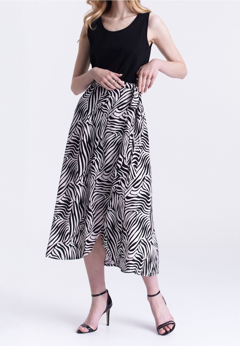 Zwart tanktop gecombineerd met een knielange, vloeiende rok met een zwart-wit zebra strepen patroon en een zijsplit. Zwarte hoge hakken.