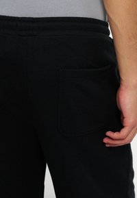 Κοντινό πλάνο ενός ατόμου που φοράει μαύρο παντελόνι με πίσω τσέπη, το χέρι ακουμπά κοντά στην τσέπη και φοράει γκρι πουκάμισο μέσα από το παντελόνι.