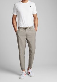 Biała koszulka z krótkim rękawem z małym czarnym logo, w połączeniu z beżowymi zwężanymi spodniami i białymi sneakersami z czerwonymi akcentami.