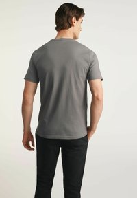 Szara bawełniana koszulka z okrągłym dekoltem, krótkimi rękawami i prostym dołem, noszona przez męskiego modela, widok z tyłu.