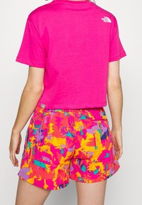 Roze crop T-shirt met korte mouwen, gecombineerd met kleurrijke shorts met patronen in roze, paars, geel en turquoise.