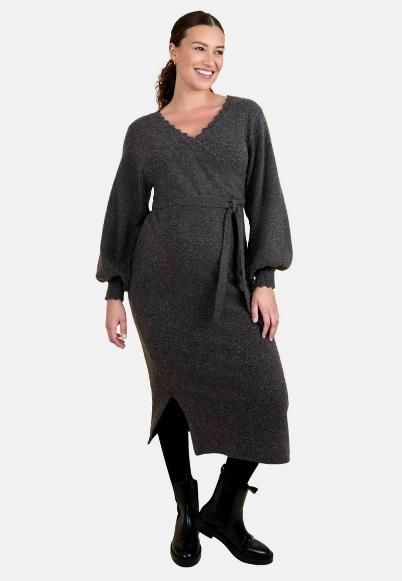 Graues Wickelkleid mit langen, ballonförmigen Ärmeln, gewelltem Ausschnitt, gebundenem Taillenbund und vorderem Schlitz, kombiniert mit schwarzen Knöchelstiefeln. Weicher Stoff.