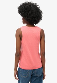 Top sin mangas de color coral con escote redondo y un ajuste ligeramente relajado, combinado con jeans de mezclilla de talle alto. Tejido suave y texturizado.