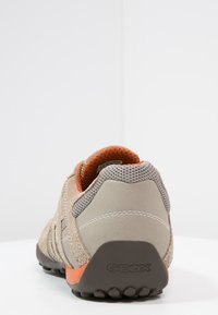 Beiga och orange Geox-sneakers visas bakifrån på en vit yta med texturerad sula och mesh-vristkrage.