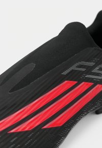 Μαύρο αθλητικό παπούτσι με κομψό σχεδιασμό, με κόκκινες διαγώνιες ρίγες και υφή στην επιφάνεια για πρόσφυση. Ελαφρύ και αεροδυναμικό σχήμα.