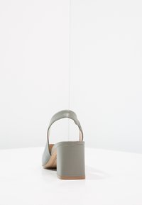 Zelené kožené sandály na vysokém podpatku s širokým blokovým podpatkem, otevřenou zadní částí a designem s náramkem na zápěstí. Hladká textura a minimalistické detaily.