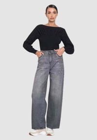 Top nero a maniche lunghe con scollo arricciato; jeans grigi a gamba larga con decorazioni scintillanti; abbinati a sneakers bianche e beige.