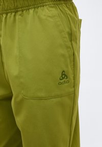 Suurplaan oliivrohelised püksid, millel on elastne vöökoht ja küljetasku, kus on tumerohelise tooniga sobituv Odlo logo.