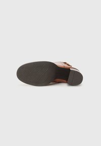 Semelle de chaussure en cuir brun avec une texture antidérapante. Présente un dessus lisse et des accents de quincaillerie décoratifs. Design plat et arrondi.