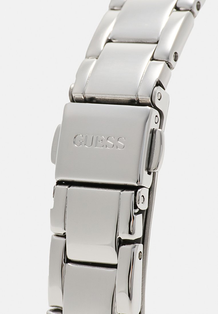 Cierre de pulsera para reloj de metal plateado pulido con el logo de GUESS grabado, mostrando eslabones detallados y mecanismo de cierre plegable.