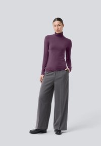 Lange mouw mock neck top in diep paars, gecombineerd met losse grijze broeken; gladde textuur, op maat gemaakte ontwerp en zwarte schoenen.