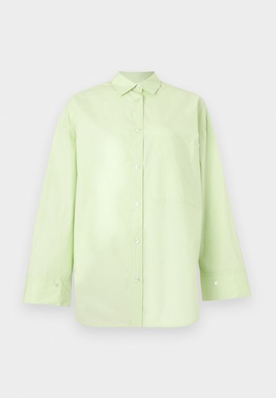 Chemise vert clair à manches longues avec boutons, col et poche poitrine, présentée sur un fond clair uni.