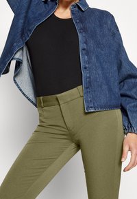 Jeansjacka i mörkblått med knäppning, bärs över en svart topp; åtsittande byxor i olivgrön med slät textur och elastisk midja.