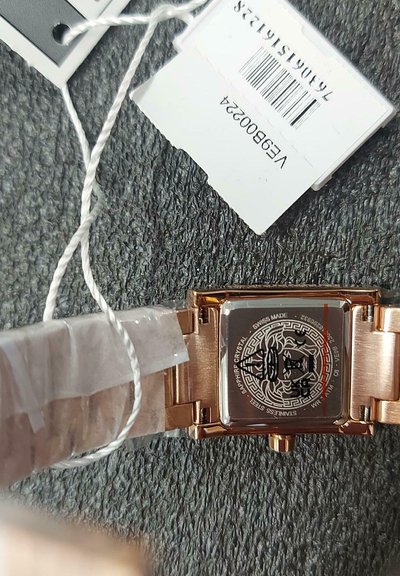 Taisnstūra formas rokas pulkstenis ar zelta krāsas nerūsējošā tērauda siksniņu. Aizmugurē ir dekoratīvs raksts un iegravēta frāze "Swiss Made".