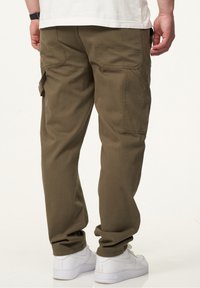 Khaki Cargo-Hosen aus Mischbaumwolle, mit großen Seitentaschen, einer lockeren Passform und aufgekrempelten Knöcheln, kombiniert mit weißen Sneakers.