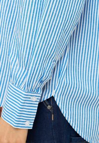 Striped blue and white long-sleeve shirt with a buttoned cuff, featuring vertical stripes and a relaxed fit.