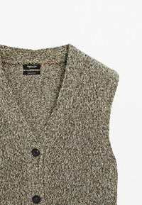 Ärmellose Strickjacke aus beigem und braun meliertem Garn mit V-Ausschnitt und zwei dunklen Knöpfen, aus 100 % Baumwolle.