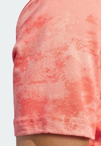 Lyhythihainen poolopaita teksturoidusta korallinvärisestä kankaasta, jossa on hienovarainen abstrakti kuvio ja perinteinen kaulussomistus.