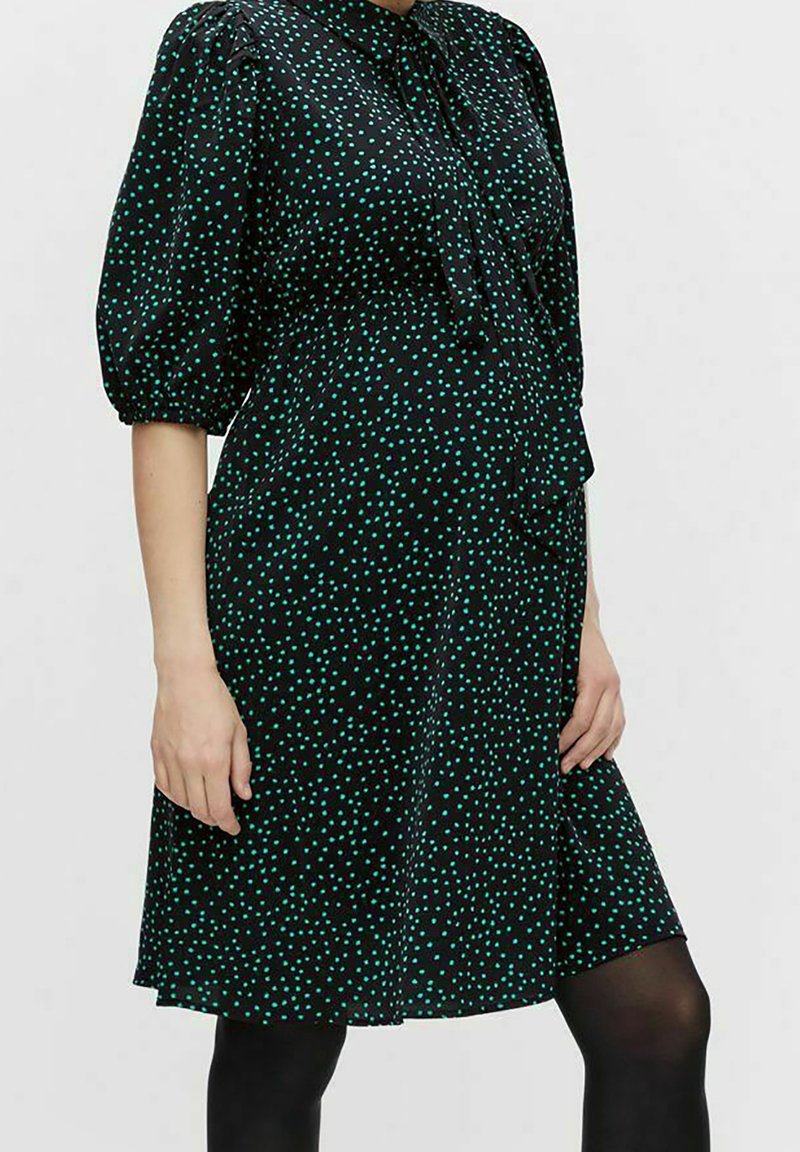 Robe noire à manches courtes bouffantes, à pois verts et rouges, avec col et nœud à l'avant, présentant une taille cintrée et une jupe évasée.