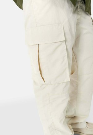 Pantalones cargo beige con múltiples bolsillos laterales, hechos de una tela ligera y texturizada. Presentan un corte holgado y detalles de costura sutiles.