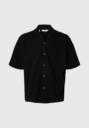 Camisa negra de manga corta con botones, cuello campestre, cinco botones visibles y un corte holgado sobre un fondo gris claro.