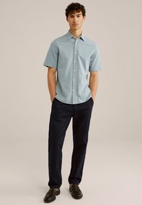 Šviesiai mėlynas trumpomis rankovėmis mygtukinis marškinėliai su subtiliu raštu; derinami su tamsiai mėlynomis kelnių ir juodais slip-on bateliais.