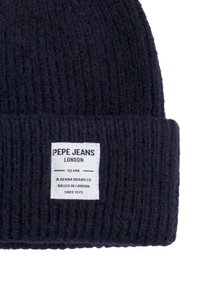 Mornarica pletena kapa s rebrastom teksturom, koja ima bijelu pravokutnu oznaku s crnim natpisom "Pepe Jeans London."