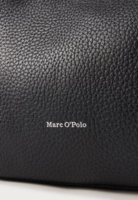 Czarna skórzana torba z fakturowaną powierzchnią i wytłoczonym białym logo "Marc O'Polo". Projekt jest minimalistyczny, bez widocznych elementów metalowych.