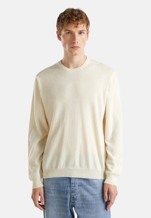 Pull à crème clair en tissu doux, avec des manches longues, un col rond et une coupe décontractée, associé à un jean bleu clair.