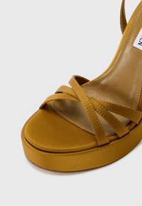 Sandalo platform giallo senape con cinturini incrociati in finitura satinata e soletta in pelle liscia. Design con punta arrotondata e suola spessa.