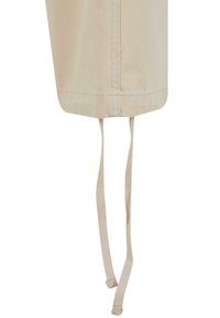 Beige stoff med en glatt tekstur, med en rund kant og to hengende bånd for justering eller feste. Enkelt design med minimal detaljering.