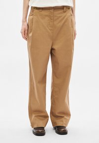 Spodnie o szerokich nogawkach wykonane z jasnobrązowej bawełny, z zamkiem błyskawicznym, dwoma przednimi kieszeniami oraz mosiężnymi guzikami na pasku.