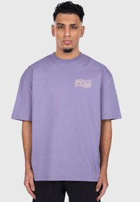 Lilac-cotton T-paita, jossa on rento istuvuus, lyhyet hihat ja pieni painettu kuosi vasemmassa rinnassa vaaleanpunaisena.