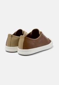 Zapatillas de cuero marrón con parte trasera de cuero claro, suela de goma blanca y cordones beige. Presentan una forma redondeada y un diseño minimalista.