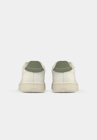 White leather sneakers with a light green suede heel tab, featuring a textured cream rubber sole and minimalistic design.