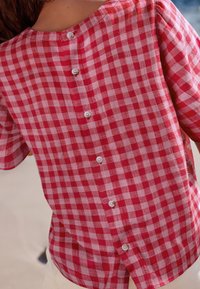 Punavalkoinen ruudullinen lyhythihainen paita, jossa on napitettu takakappale, kevyt kangas ja pyöreä pääntie. Napit näkyvissä selvästi.