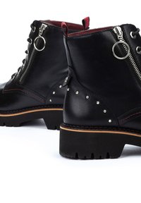 Black leather ankle boots with a textured finish, featuring zippers, metal accents, red lining, and a sturdy treaded sole.
