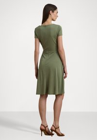 Vestido verde até aos joelhos com mangas curtas, corpete ajustado e saia larga. Apresenta um fecho de correr nas costas e um tecido liso e elástico.