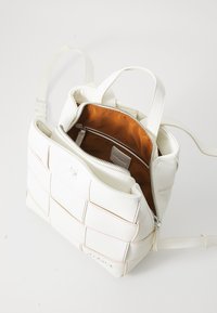 Borsa bianca con una trama intrecciata, dotata di zip superiore, interno arancione e tasca interna. Inclusi anche manici regolabili.