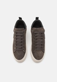 Tmavě šedé semišové tenisky s nízkým designem, se plochými tkaničkami, krémovou gumovou podešví a černým podšívkou na límci.