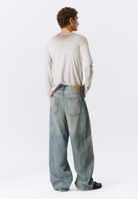 Ανοικτό γκρι μακρυμάνικο πουκάμισο σε συνδυασμό με φαρδιά ανοιχτό μπλε τζιν παντελόνια με ξεθωριασμένο εφέ, τσέπες μπροστά και πίσω, και καφέ ετικέτα στη μέση.