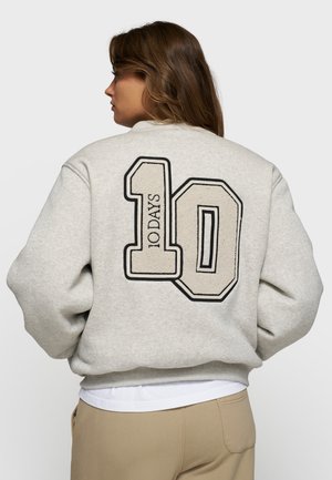 Felpa grigia con vestibilità oversize, caratterizzata da un ampio logo ricamato "10 DAYS" in crema e nero sul retro. Texture morbida, polsini a costine.