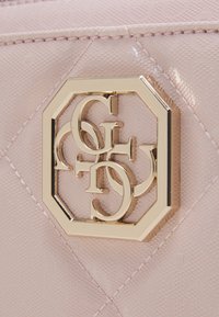 Materiale rosa testurizzato con un motivo trapuntato, con un logo ottagonale dorato al centro, caratterizzato da lettere interconnesse.