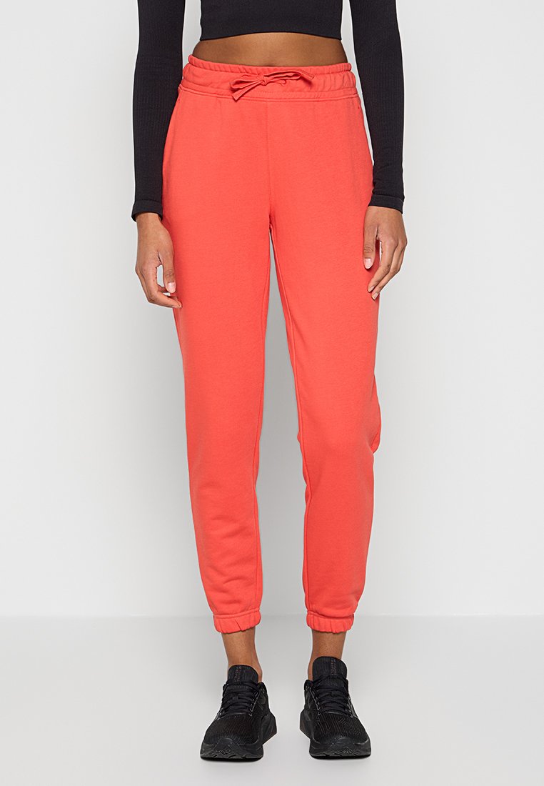 Schmal geschnittene Korallen-Jogginghosen mit elastischen Bündchen und Kordelzugbund, getragen mit schwarzen Laufschuhen und einem schwarzen Langarm-Crop-Top.