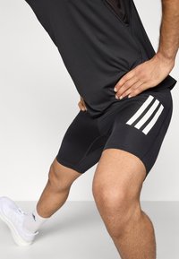 Schwarze Sportshorts mit weißem Drei-Streifen-Muster an der Seite, aus elastischem Material gefertigt, entworfen für Komfort und Bewegungsfreiheit.