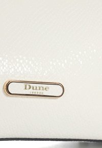 Sac à main texturé blanc avec une plaque logo Dune London en métal doré. Surface lisse avec un motif subtil, complétée par des accents noirs.