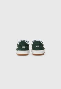 Ténis Vans verdes de camurça com costuras brancas, sola de borracha de goma e colarinho acolchoado. Apresenta o logo na parte de trás. Vista traseira.